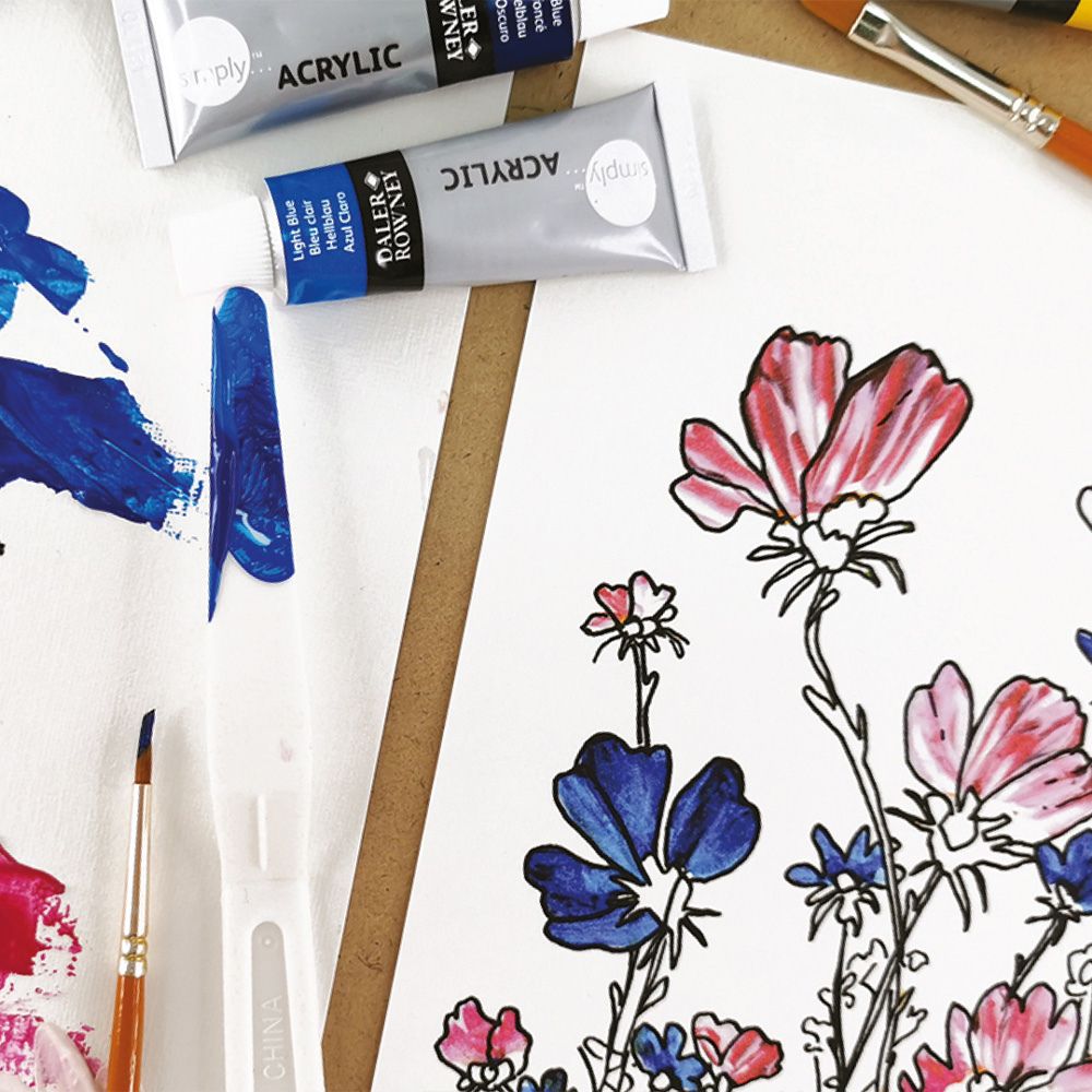Art supplies including acrylic paint tubes and brushes on a white surface with floral drawings.